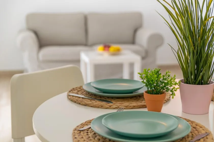 A bright sitting area with a white table set with green plates and potted plants.