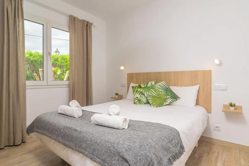A bright bedroom with a bed dressed in white and green leaf-patterned pillows.