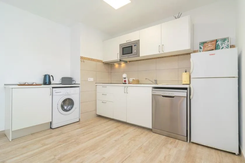A compact kitchen with white cabinets, a refrigerator, and stainless steel appliances.