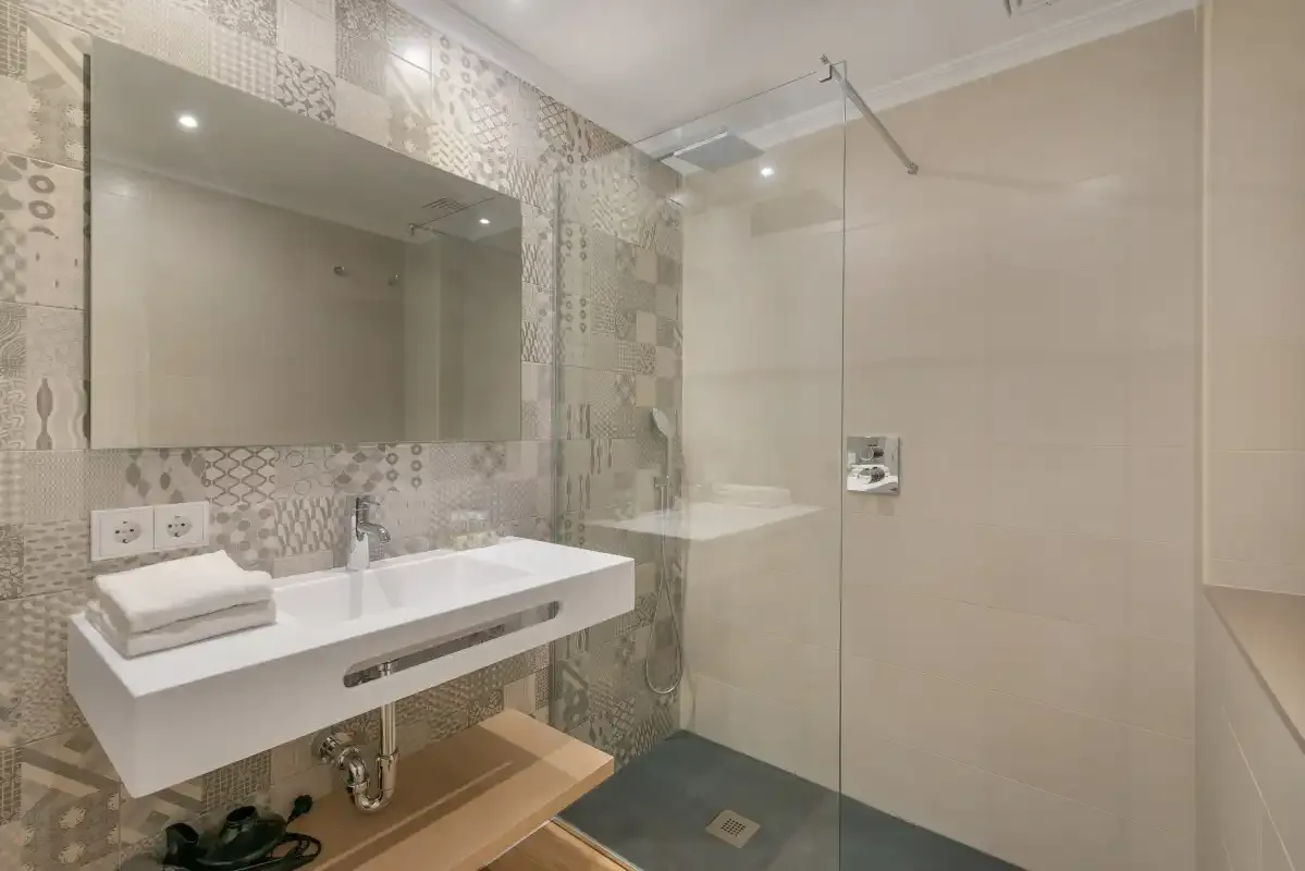 A tiled bathroom with a sink, mirror, and glass shower.