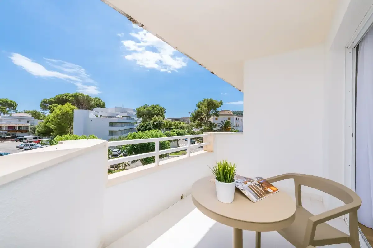 A bright balcony seating area overlooks nearby buildings and trees.