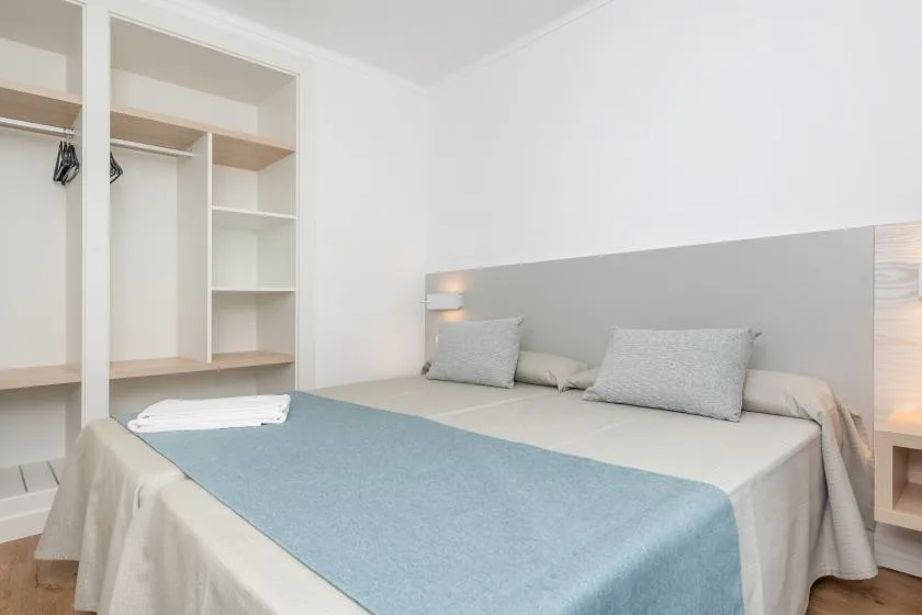 A bedroom with a bed made with pale bedding and a blue cover.