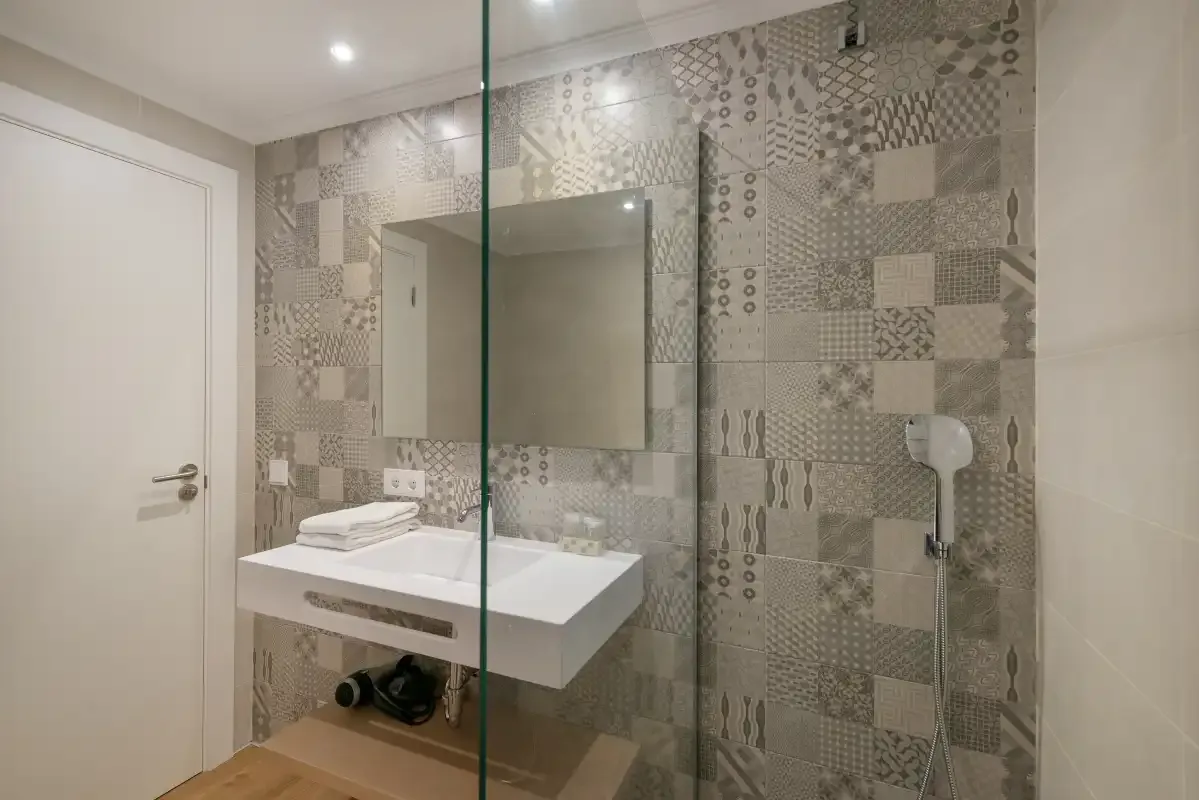 A bathroom with a wall-mounted sink and patterned tiled walls.