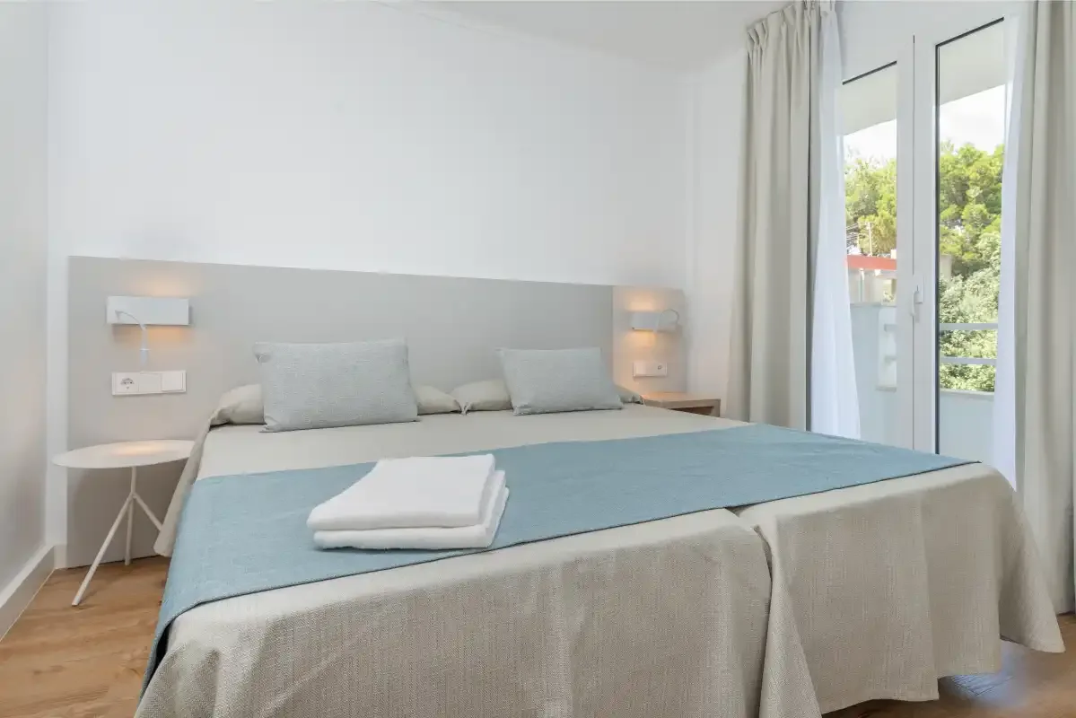 A bright bedroom with a neatly made bed beside tall windows.