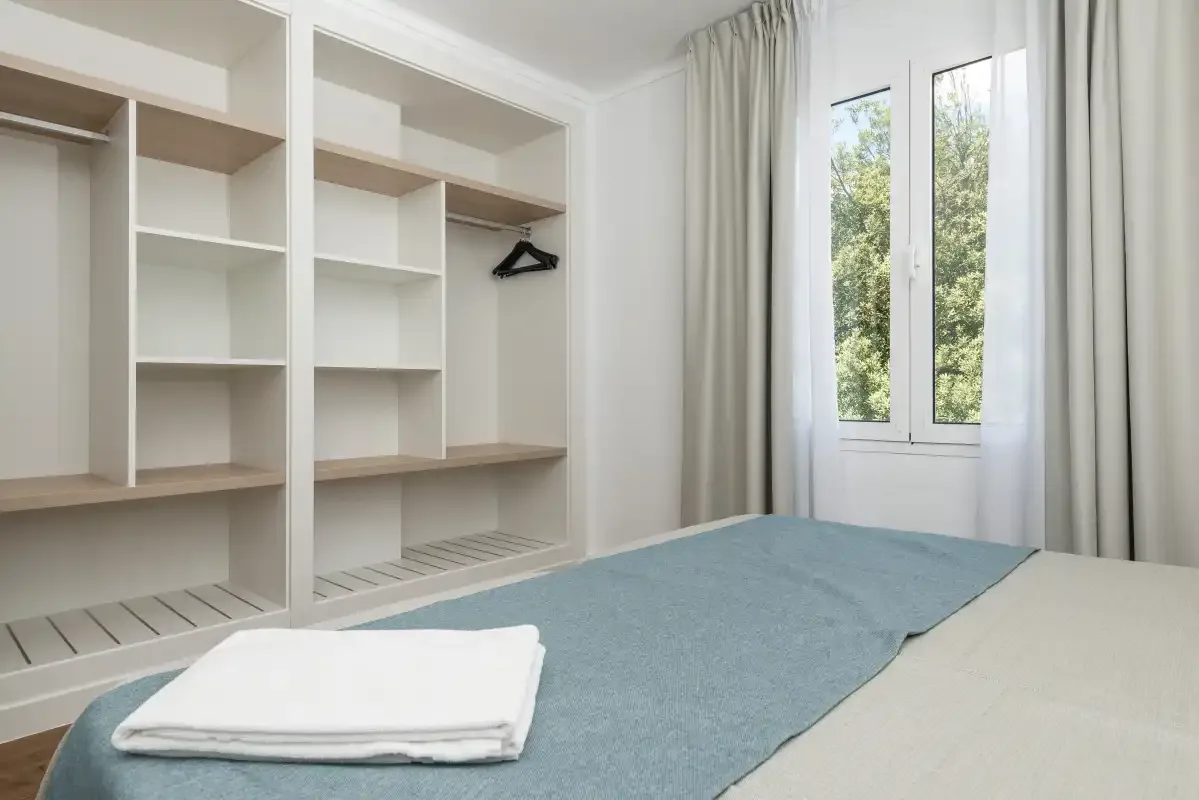 A bedroom with built-in shelving, a bed, and a window.