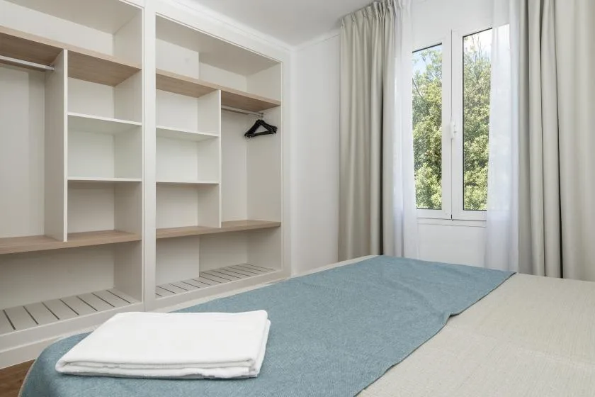 A bedroom with a bed, open shelving, and a curtained window.