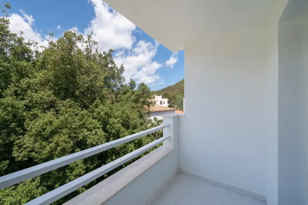 A white balcony overlooks leafy trees and a distant hillside.