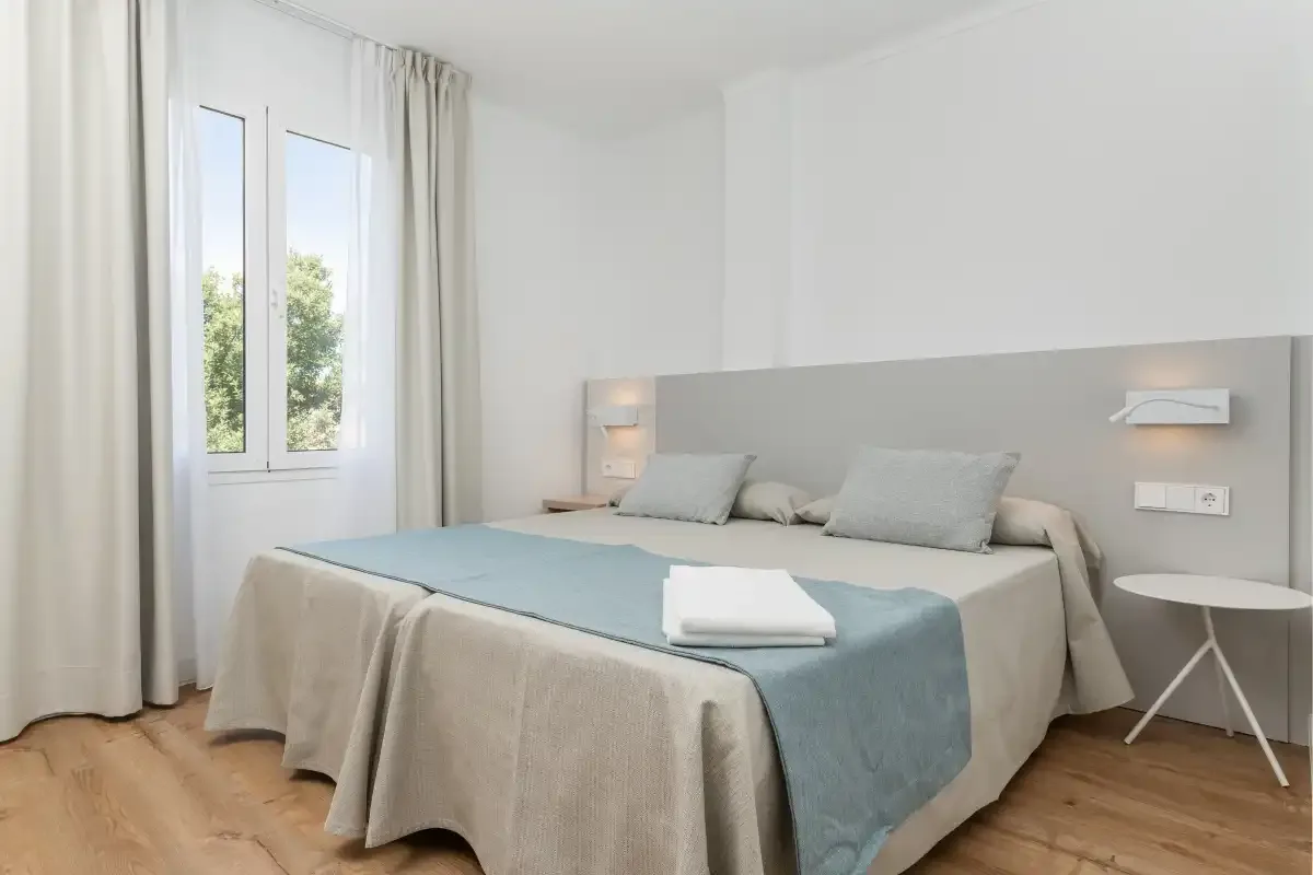 A bright bedroom with a neatly made bed beside a window.