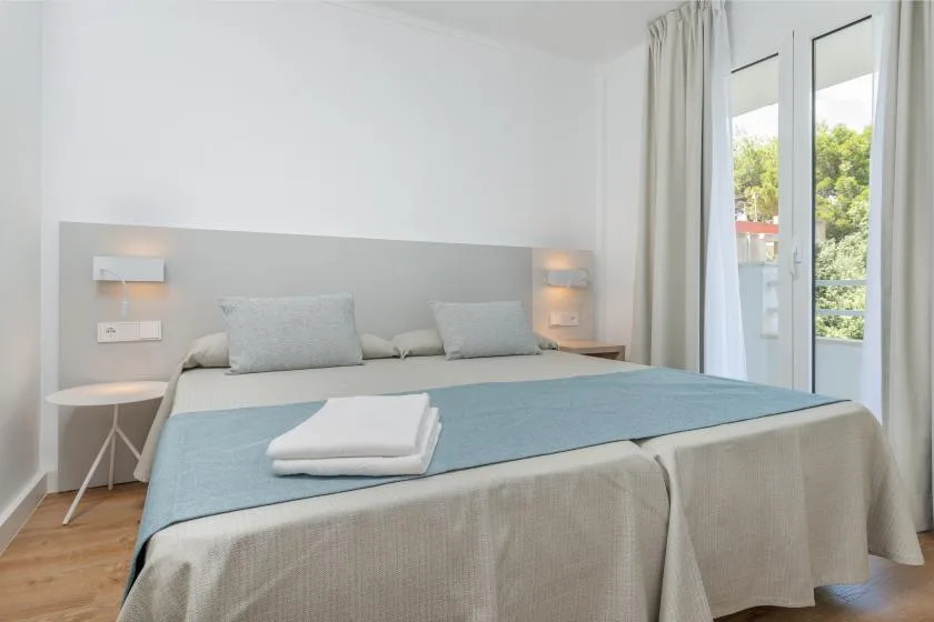 A bright bedroom with a neatly made bed and glass doors opening to a balcony.