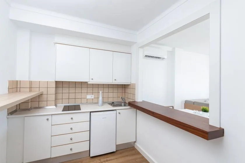 A compact kitchen with white cabinets, tiled backsplash, and a wooden counter.