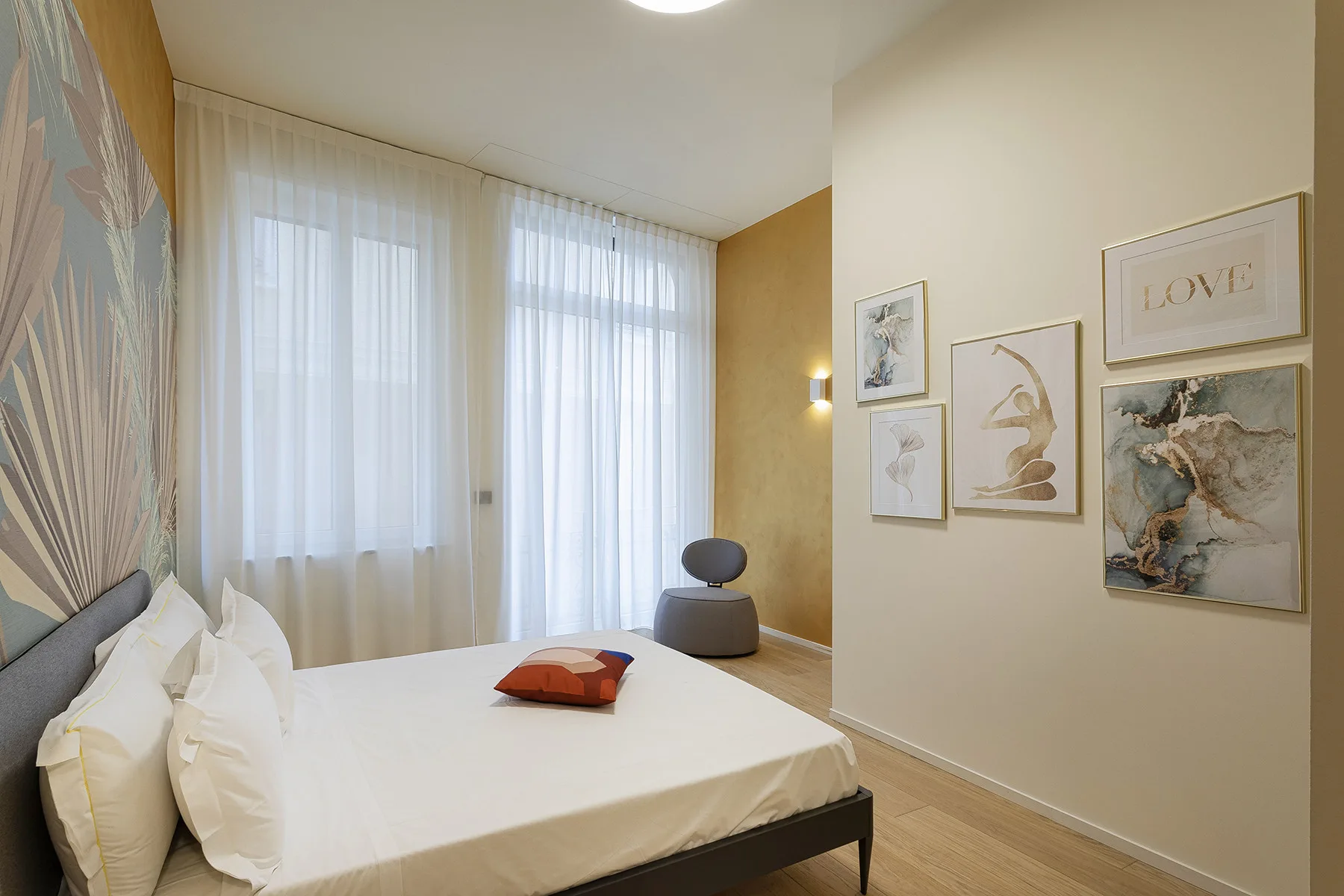 A bedroom with a bed, sheer curtains, and framed wall art.
