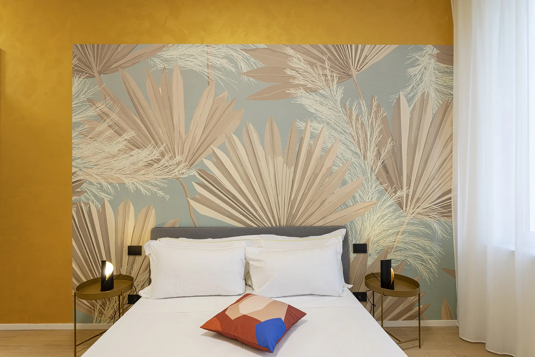 A bedroom with a white bed against a wall decorated with a large botanical mural.