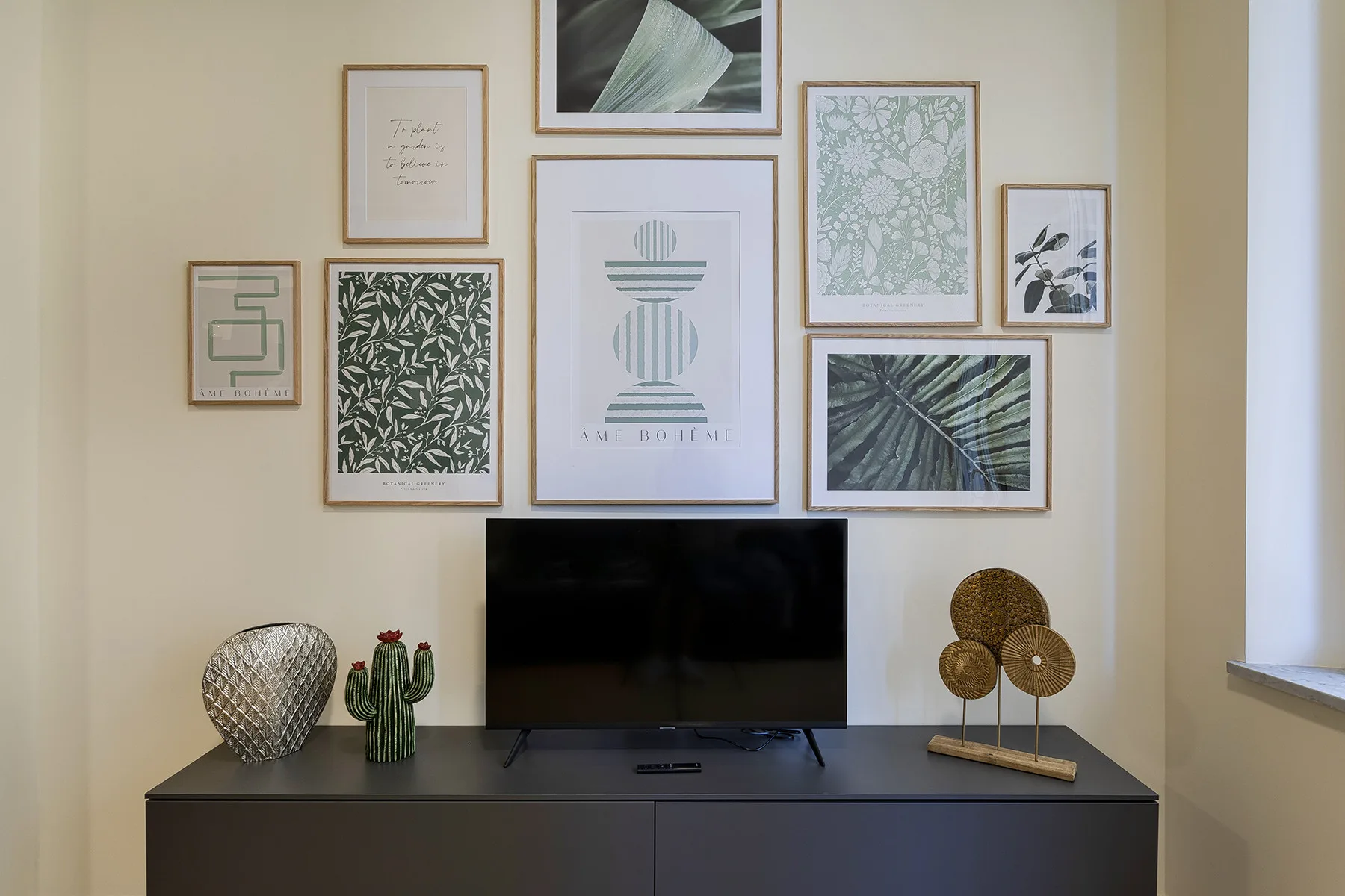 A television sits on a dark cabinet beneath a wall of framed botanical prints.