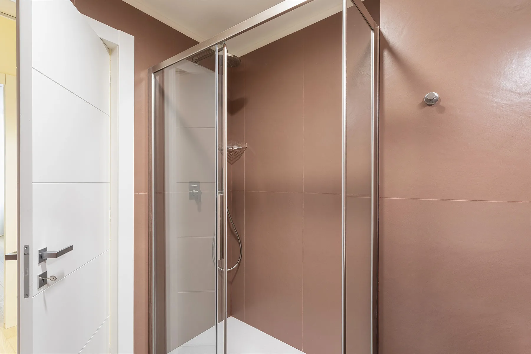 A bathroom shower with glass panels and brown walls.