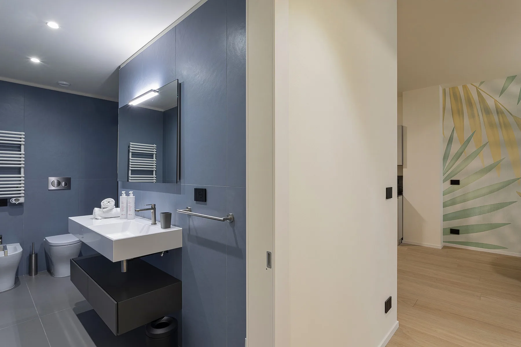 A modern bathroom with a wall-mounted sink and dark blue walls.