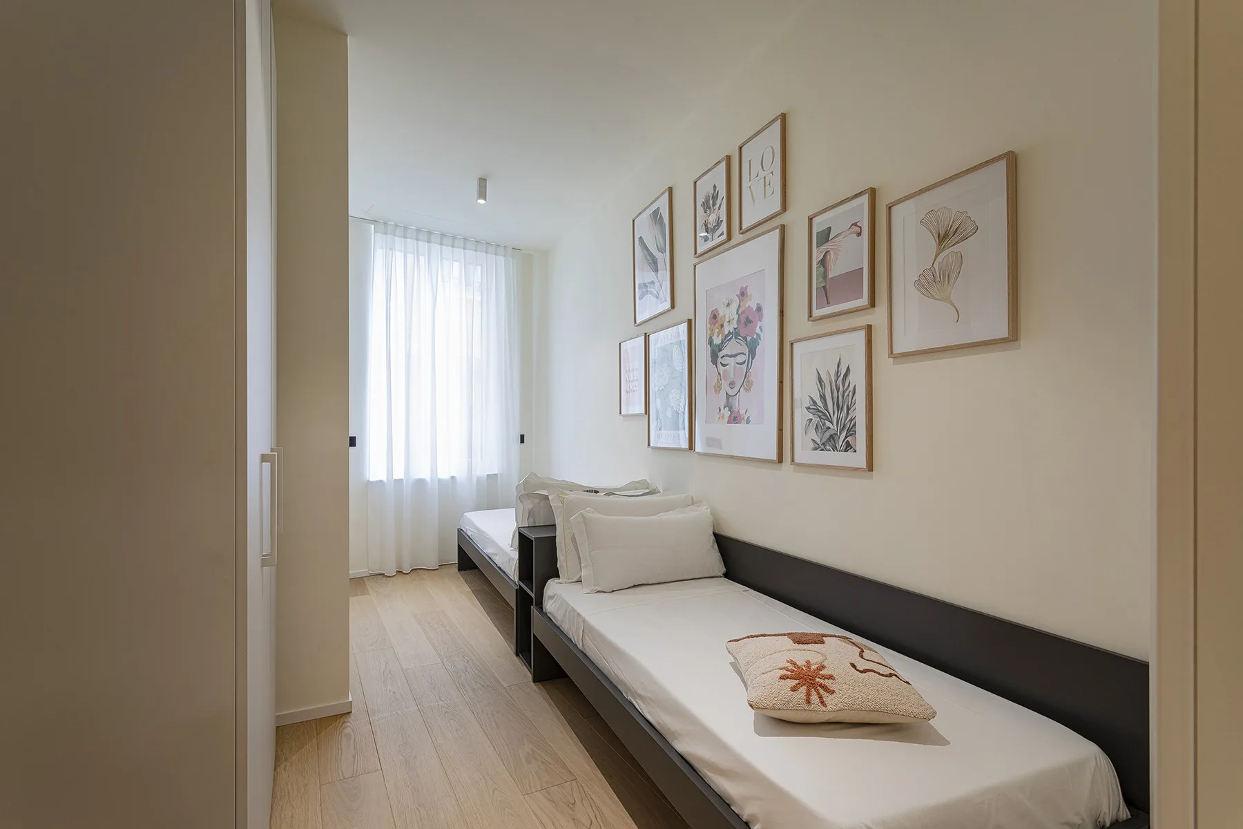 A bright bedroom with two single beds and framed artwork on the wall.
