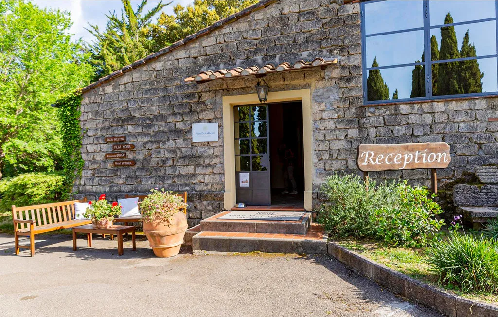 Stone building entrance with a reception sign and a bench beside potted plants.