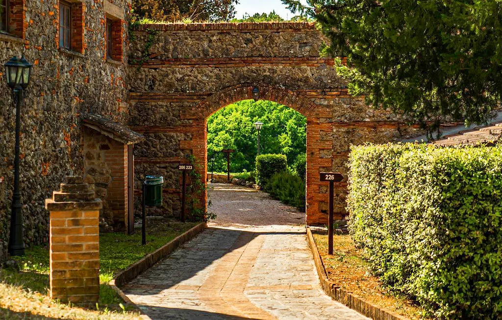 A stone entrance arch frames a paved path bordered by greenery.