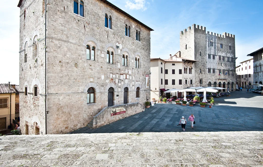 A paved town square is bordered by historic stone buildings and outdoor café seating.