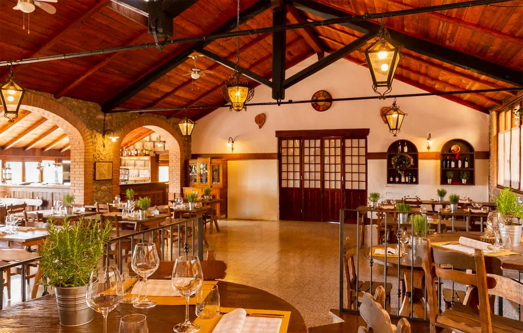 A warmly lit restaurant dining room with wooden tables and exposed ceiling beams.