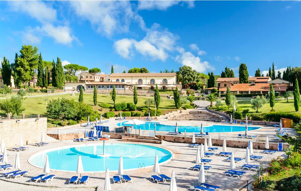 Zona de piscina al aire libre con tumbonas, jardines y edificios al fondo.
