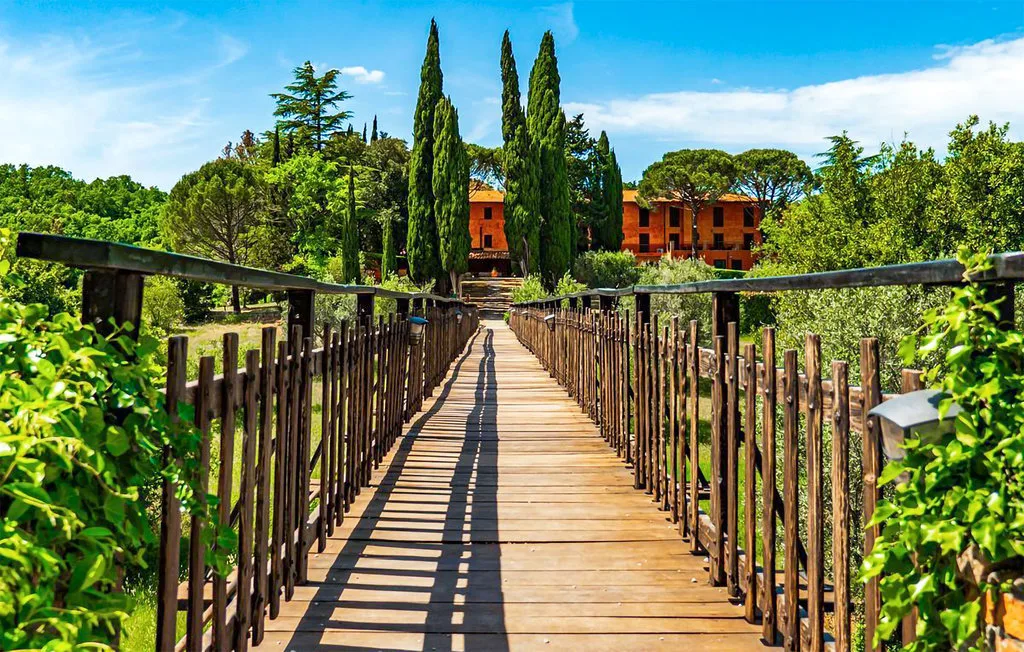 Una pasarela de madera cruza jardines verdes hacia un edificio rojo.