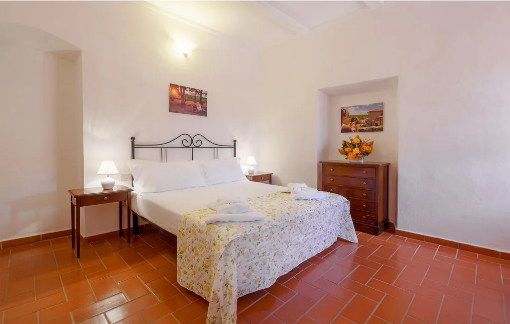 Bedroom with a bed, bedside tables, and terracotta-colored floor tiles.