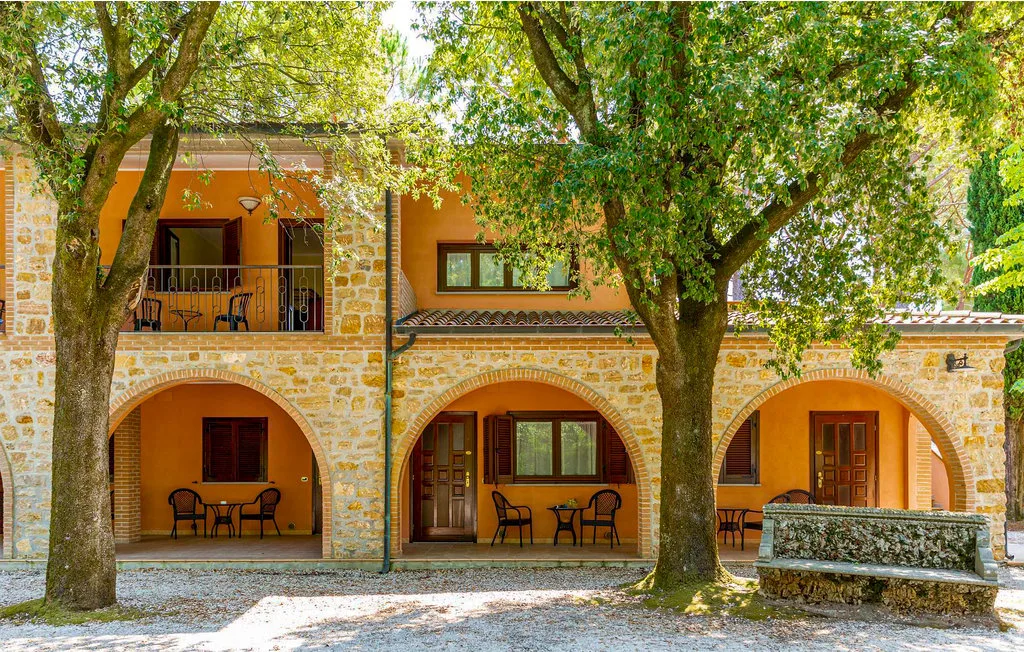 A stone-and-orange building with arched patios beneath leafy trees.