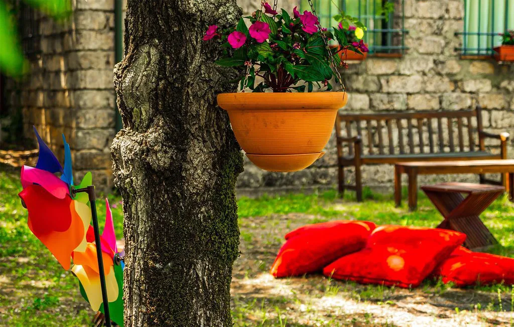 A garden seating area features a tree, colorful flowers, and bright cushions.