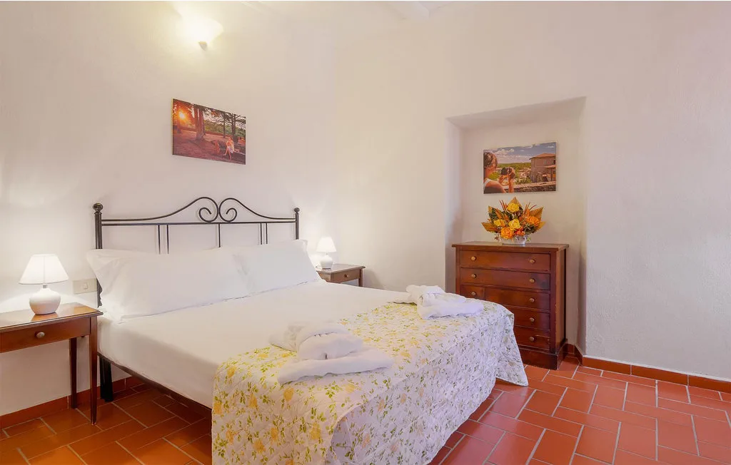 A bedroom with a double bed, floral bedding, and a wooden dresser.