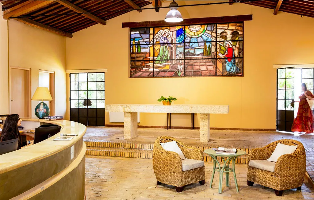A spacious lobby features a curved reception desk and wicker seating beneath a stained-glass window.