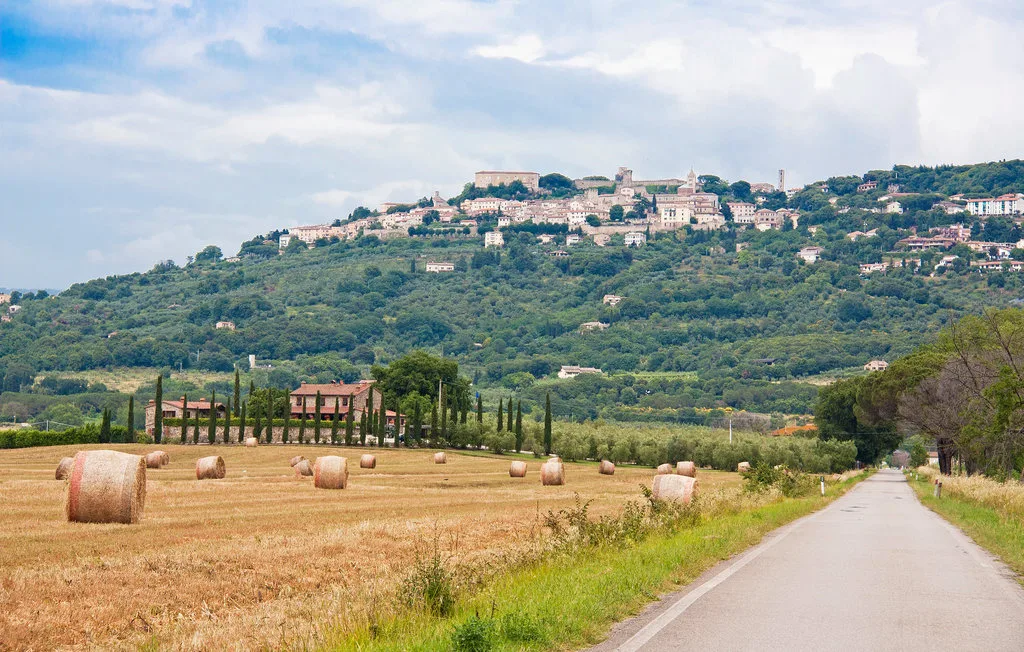 A paved country road passes harvested fields below a hillside town.