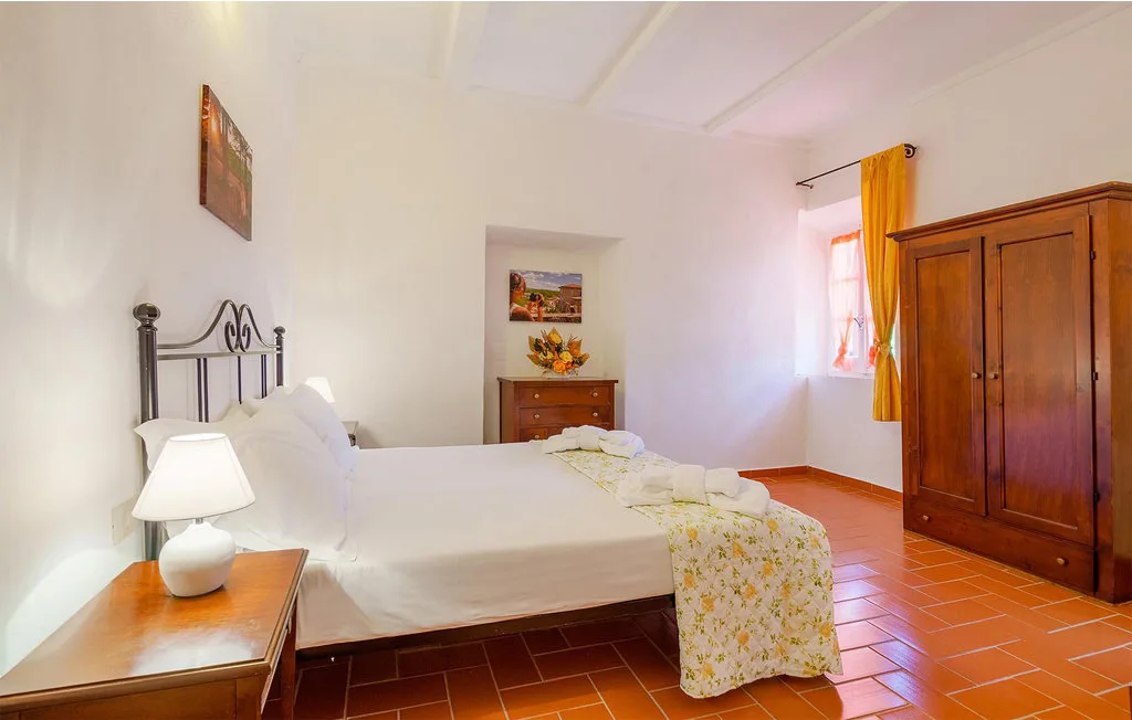 A bedroom with a neatly made bed, bedside table, and wooden wardrobe.