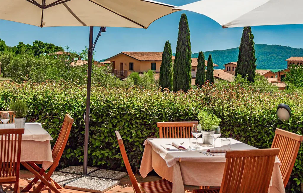 Outdoor dining area with tables beneath umbrellas, overlooking greenery and hills.