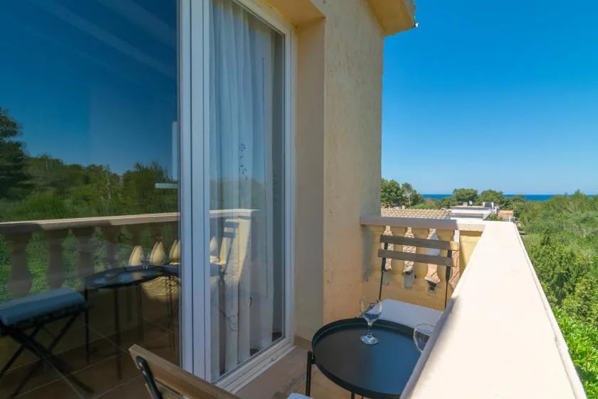 A balcony with a small round table and views of greenery and the sea.