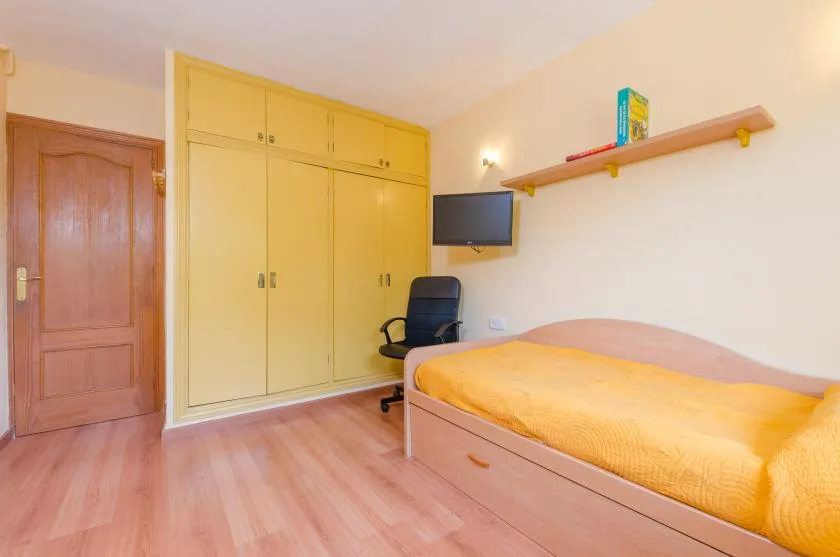 A bedroom with a bed, built-in cupboards, and a small wall-mounted television.
