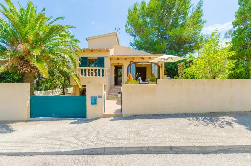 A yellow house behind a low wall, with a palm tree and gated entrance.
