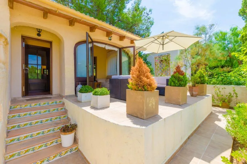 A sunny outdoor patio with potted plants, seating, and a large umbrella.