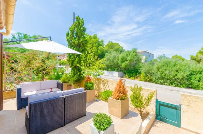 A sunny outdoor patio with seating, potted plants, and a large shade umbrella.