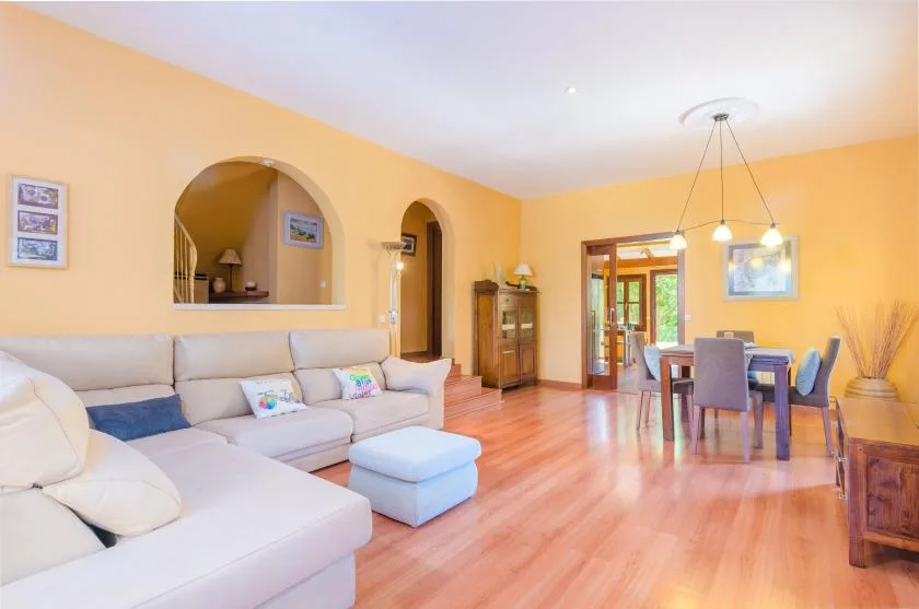 A bright living and dining room with pale seating and a wooden dining table.