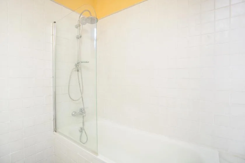 A tiled shower area with a glass panel and handheld showerhead.