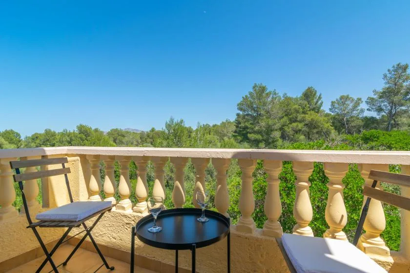 A sunny outdoor balcony with seating and a view of trees under a clear sky.