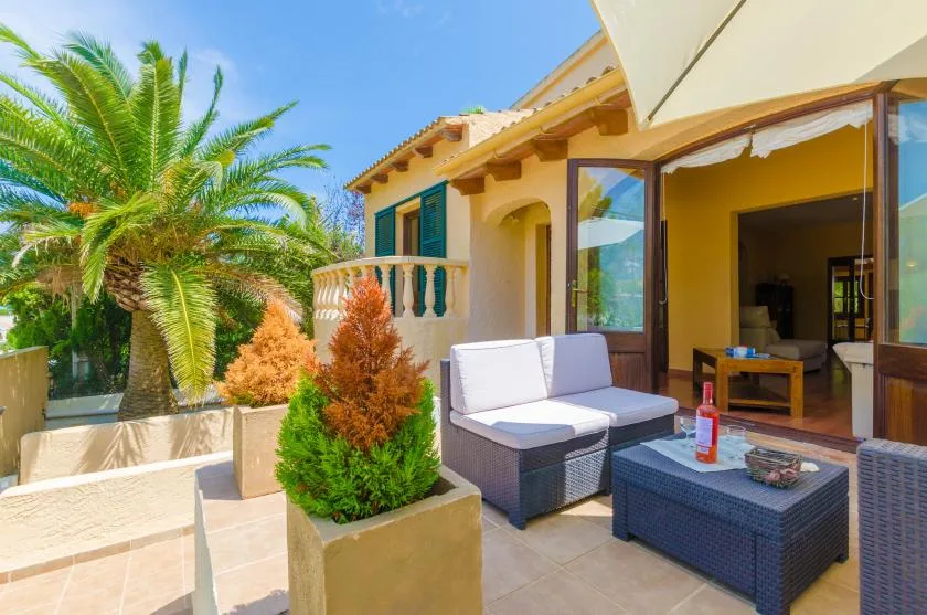 Un patio soleado con asientos exteriores y puertas abiertas a una habitación interior.