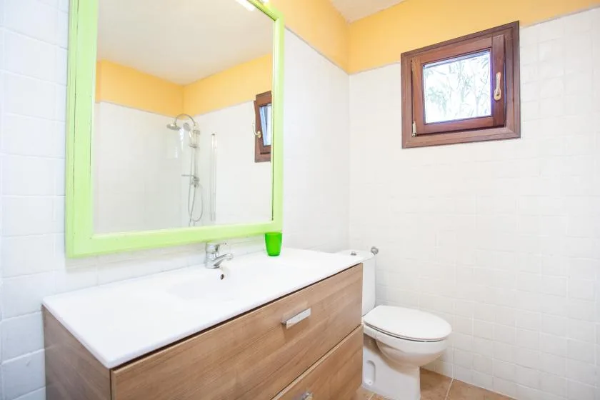 A bathroom with a vanity, mirror, toilet, and small window.
