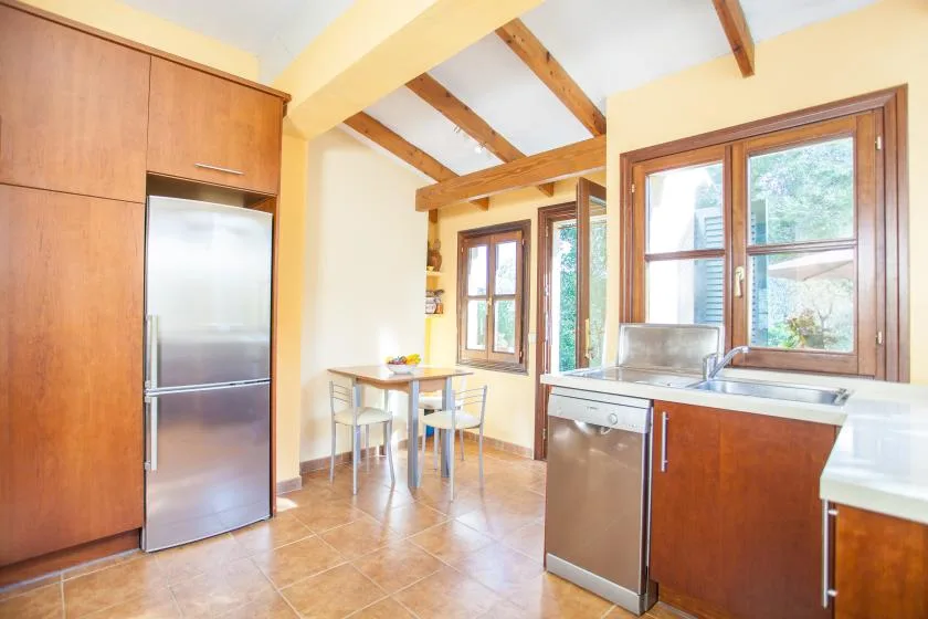 A bright kitchen with wooden cabinets, a dining table, and large windows.