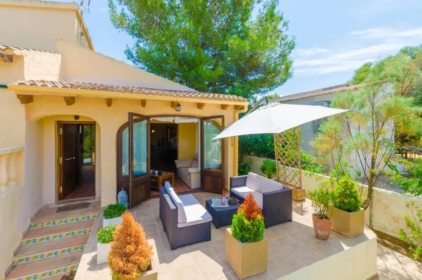A sunny outdoor patio with seating, potted plants, and a large shade umbrella.