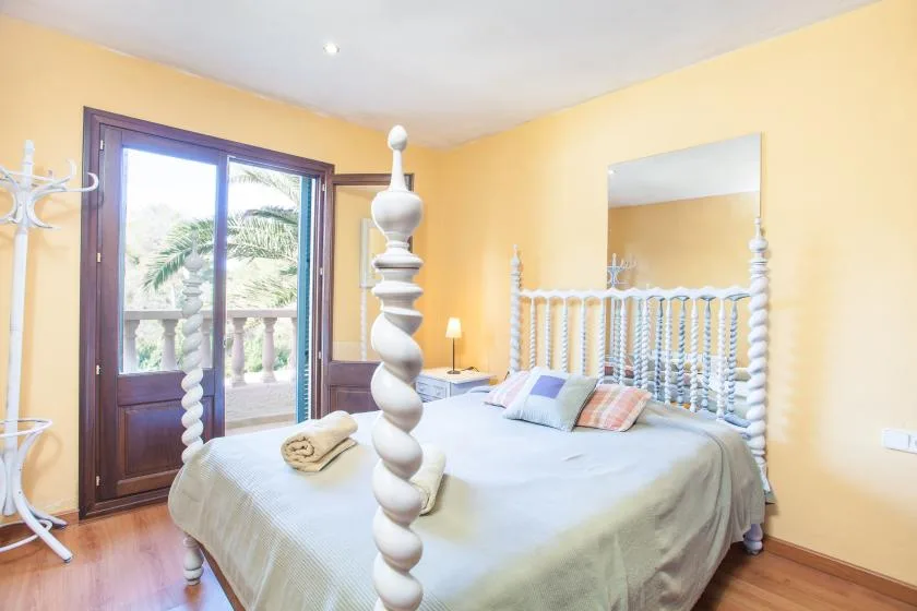 A bedroom with a large bed, decorative headboard, and windows overlooking greenery.
