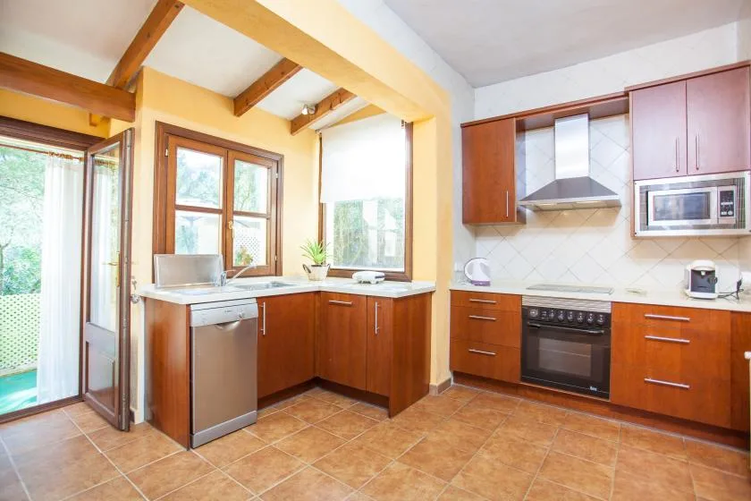 A bright kitchen with wooden cabinets, a countertop, and exposed ceiling beams.