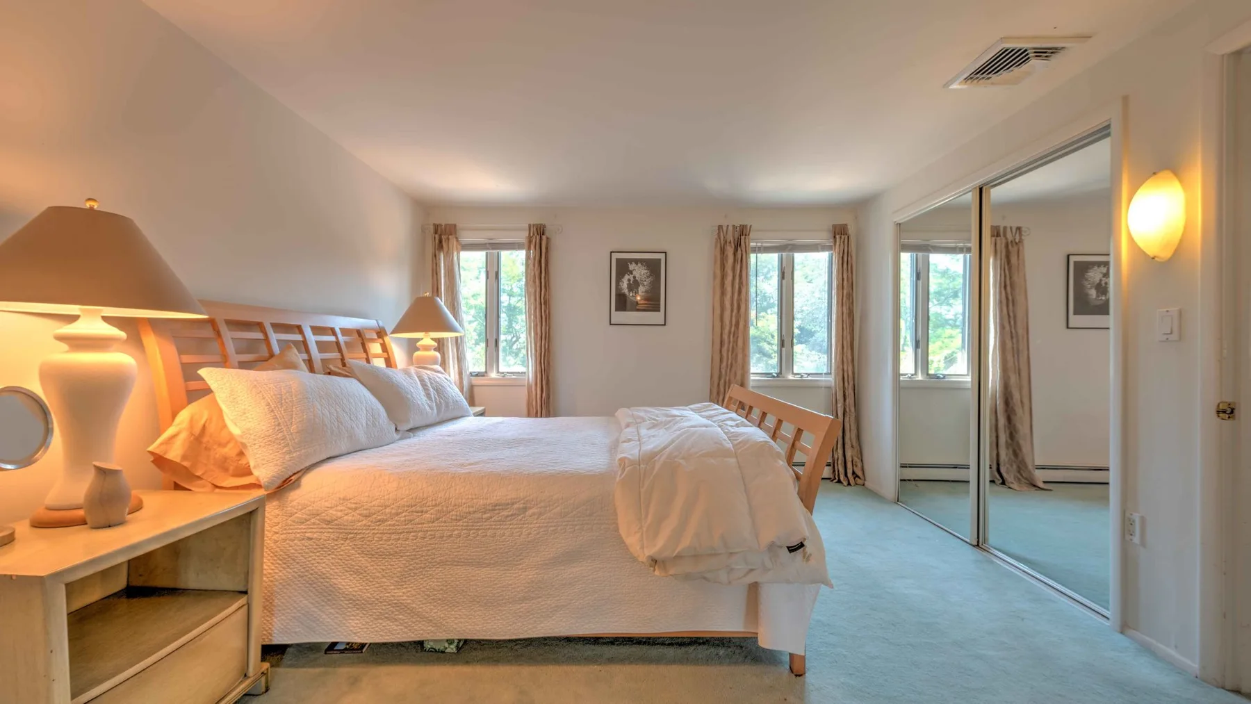A bedroom with a large bed, bedside tables, and windows overlooking greenery.
