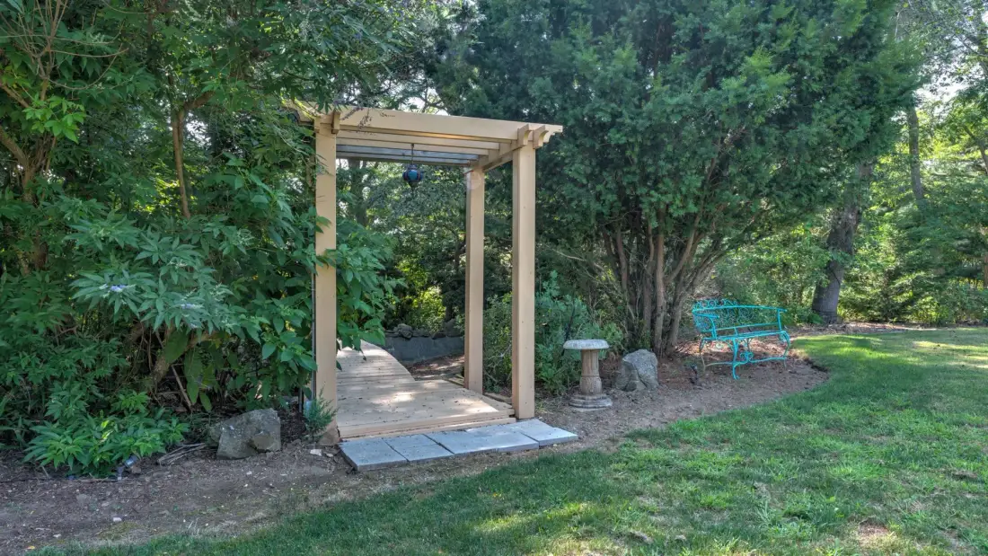 A garden path passes through a wooden arbor beside a bench.